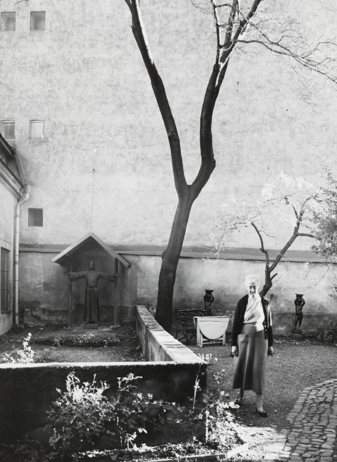 Konstnärinnan Louise Adelborg under vårdlinden på gården Grev Turegatan 68. Edelweisskapellet skymtar till vänster